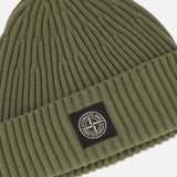 A military green STONE ISLAND Ribbed Wool Beanie with a folded cuff, featuring a black rectangular patch with the signature Stone Island compass logo on the front.