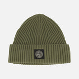 STONE ISLAND’s Ribbed Wool Beanie in olive green features a folded brim and showcases a black and white circular logo patch at the front center. This classic military green accessory stands out against a plain white background.