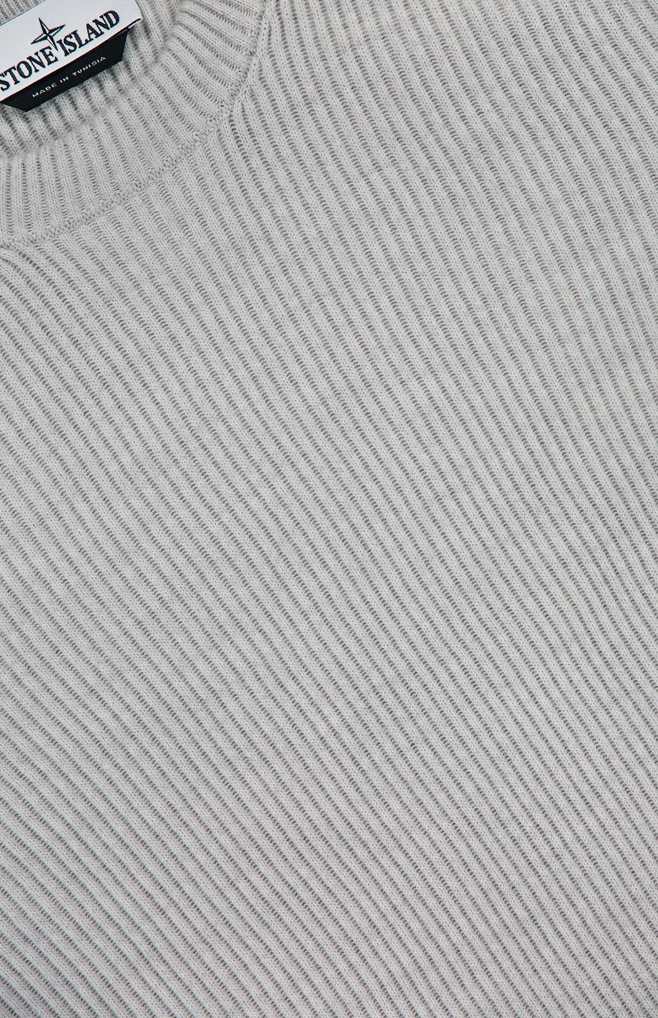 A close-up of the STONE ISLAND Ribbed Crewneck Sweater in light gray, featuring a ribbed knit design and a visible brand label near the collar.