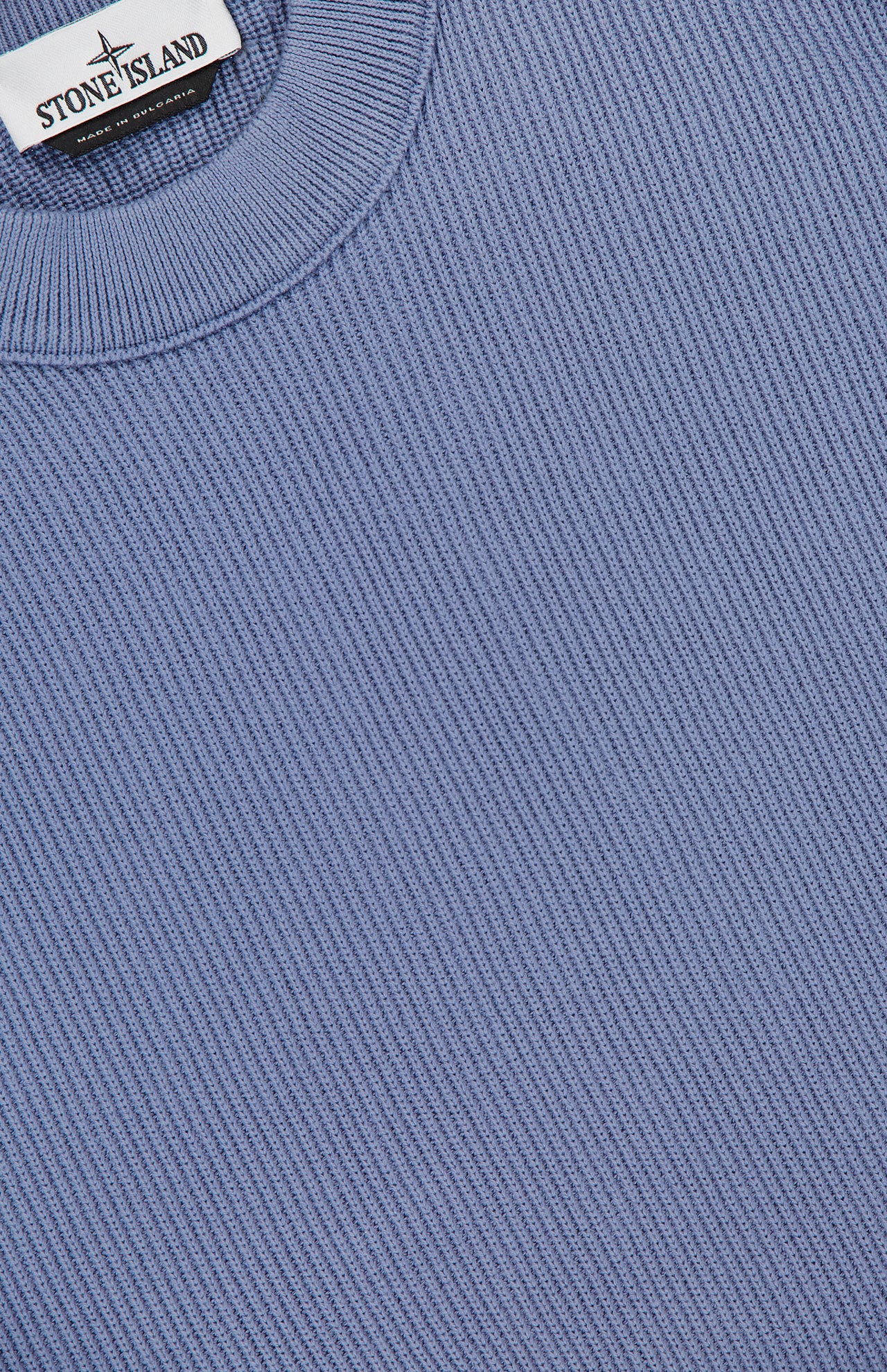 Close-up of a light blue STONE ISLAND Ribbed Knit Crewneck Sweater featuring a cotton ribbed knit design and the iconic label near the collar.