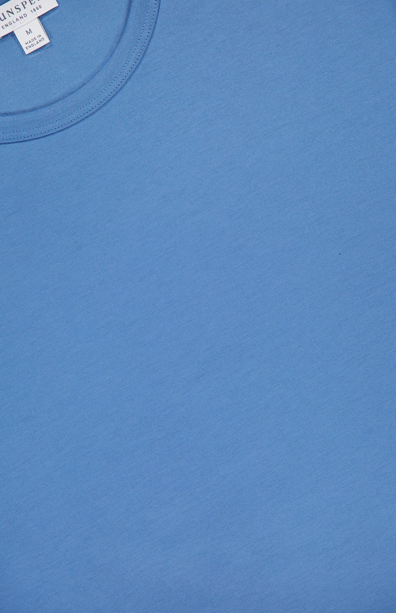 A close-up of the SUNSPEL Classic Short Sleeve T-shirt in blue highlights the crew neck collar and a white label displaying sizing and brand details in the upper left corner.