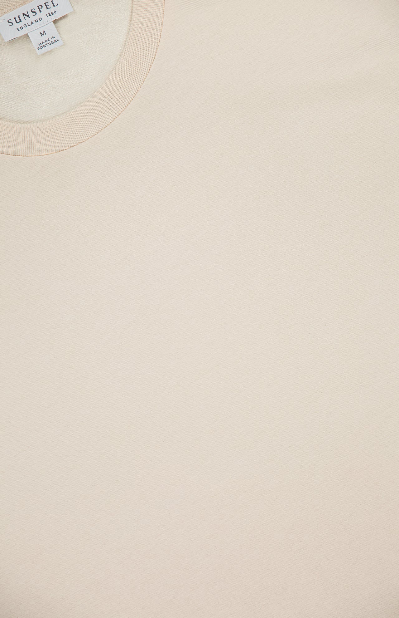 Close-up of SUNSPEL's Classic Short Sleeve T-Shirt in light beige, laid flat to showcase its smooth, soft cotton fabric. The collar and label with brand and size are visible; this timeless tee is crafted in Portugal.