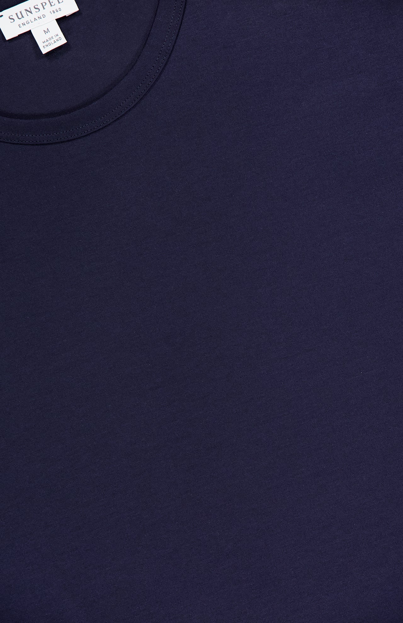 A close-up of the SUNSPEL Long Sleeve Classic T-Shirt, made from 100% cotton, showing part of the collar and a white tag with brand name and size. The smooth navy blue fabric highlights its soft quality.