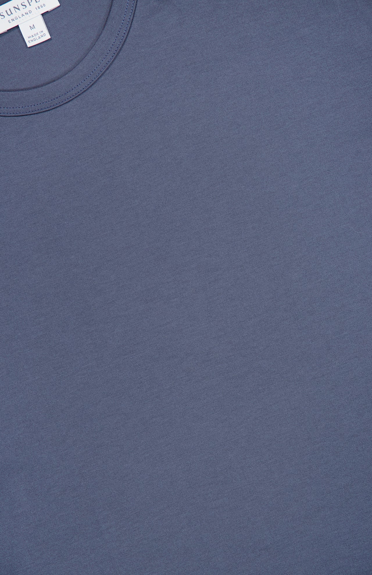 A close-up of the SUNSPEL Short Sleeve Classic T-Shirt in blue, laid flat to highlight its smooth cotton texture, round neckline, and visible size tag near the top left.