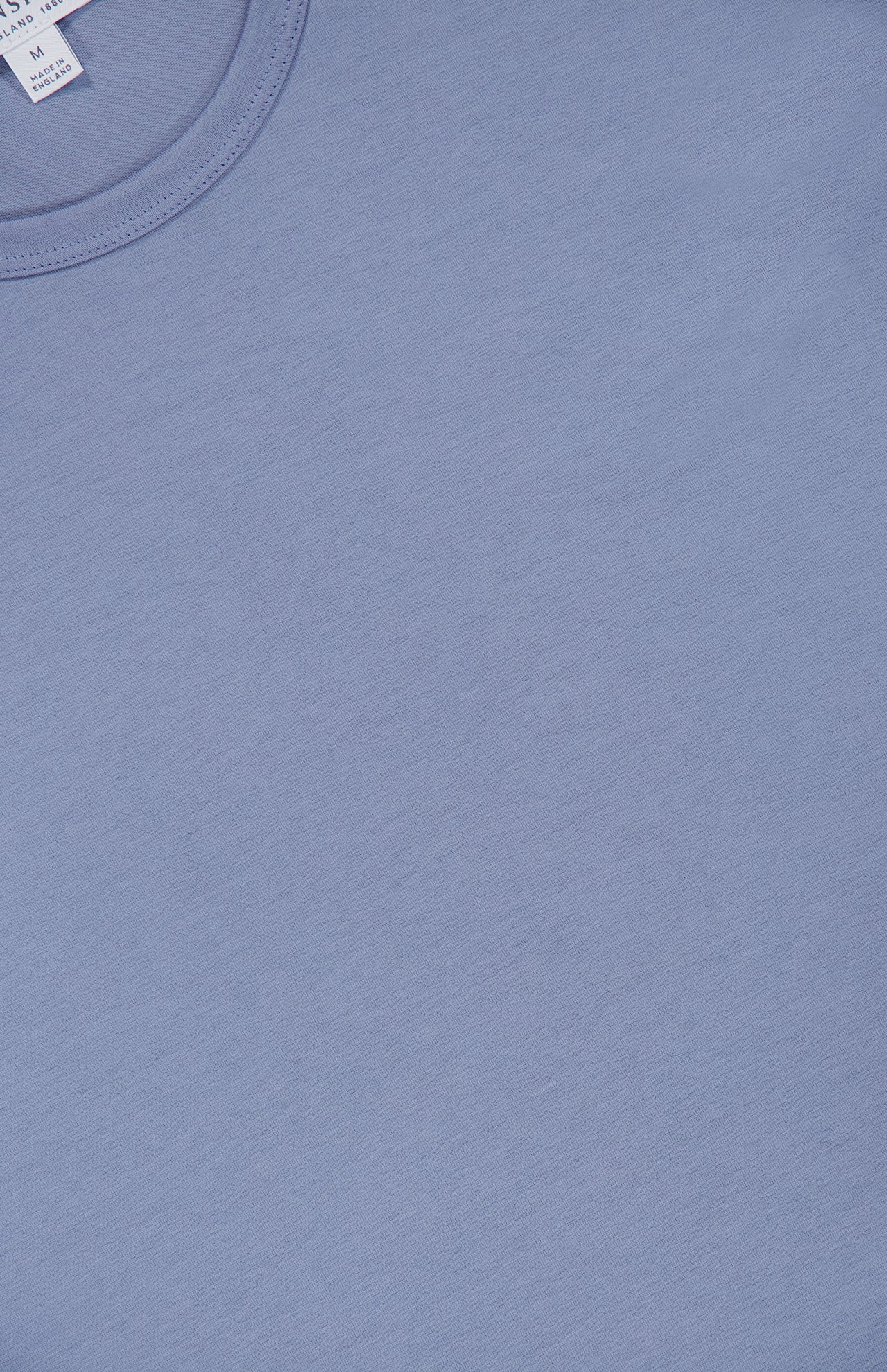 A close-up of the SUNSPEL Short Sleeve Classic T-Shirt in light blue cotton, highlighting the collar and part of the tag. Made in England, this timeless tee has a simple, understated style with no visible designs or patterns.