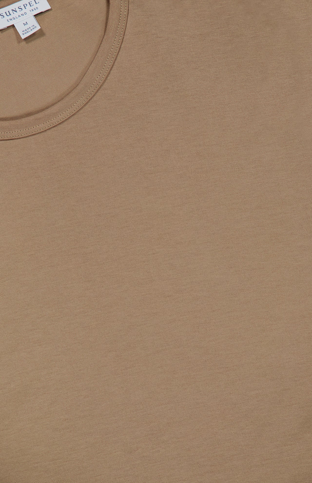 Close-up of the SUNSPEL Short Sleeve Classic T-Shirt in a plain, light brown or camel shade, laid flat. The neckline and part of a white clothing label with text—showing it is made in England—are visible in the upper left corner.
