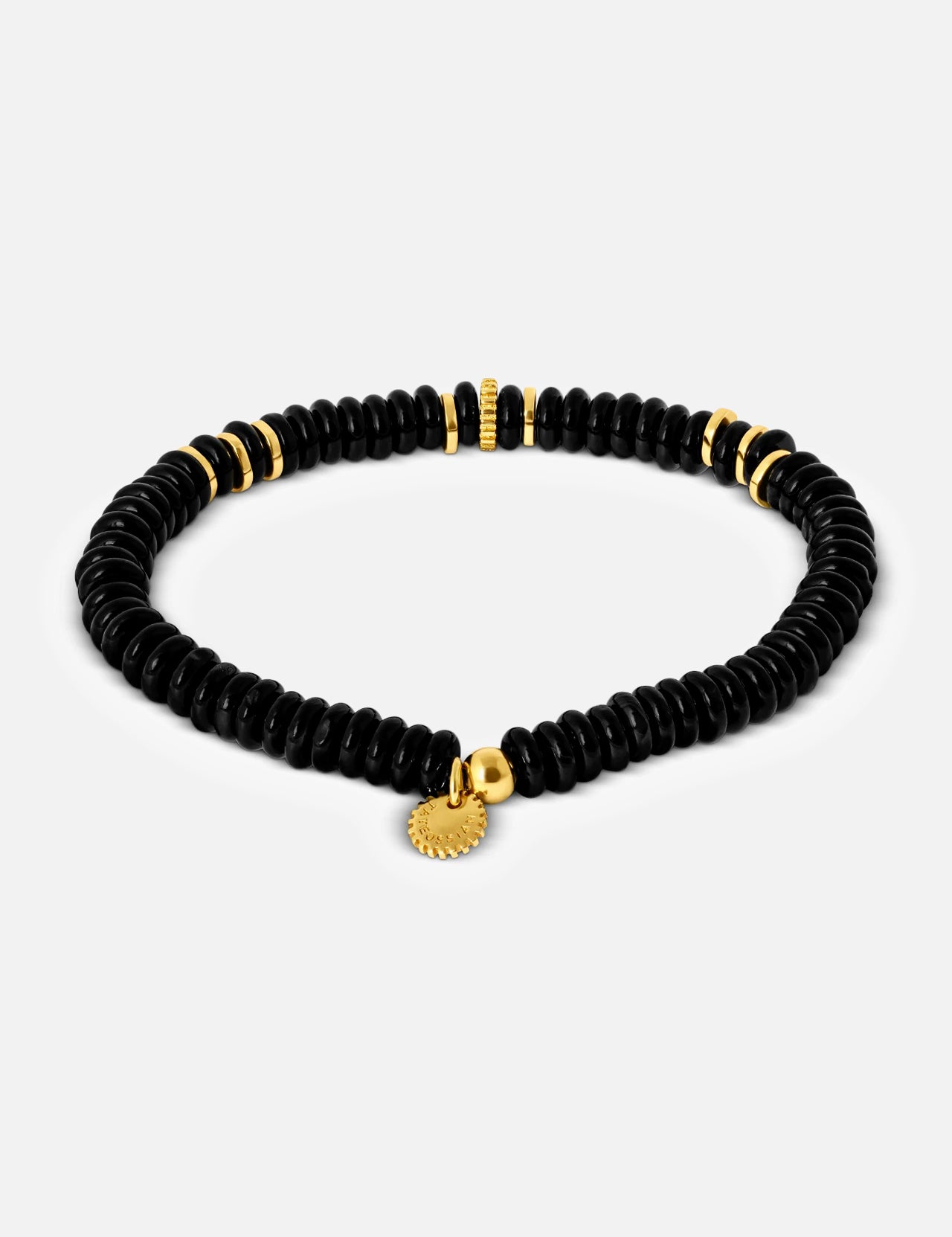The TATEOSSIAN Black Agate Bracelet showcases disc-shaped black agate beads, small gold accents, and a gold charm, presented on a plain light background.