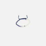 The TATEOSSIAN Feng Shui Fish Macrame Bracelet features blue and white cords, blue sodalite beads, a small metal bar, and an evil eye charm at the center, shown against a plain white background.