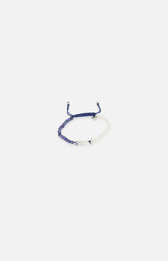 The TATEOSSIAN Feng Shui Fish Macrame Bracelet features blue and white cords, blue sodalite beads, a small metal bar, and an evil eye charm at the center, shown against a plain white background.