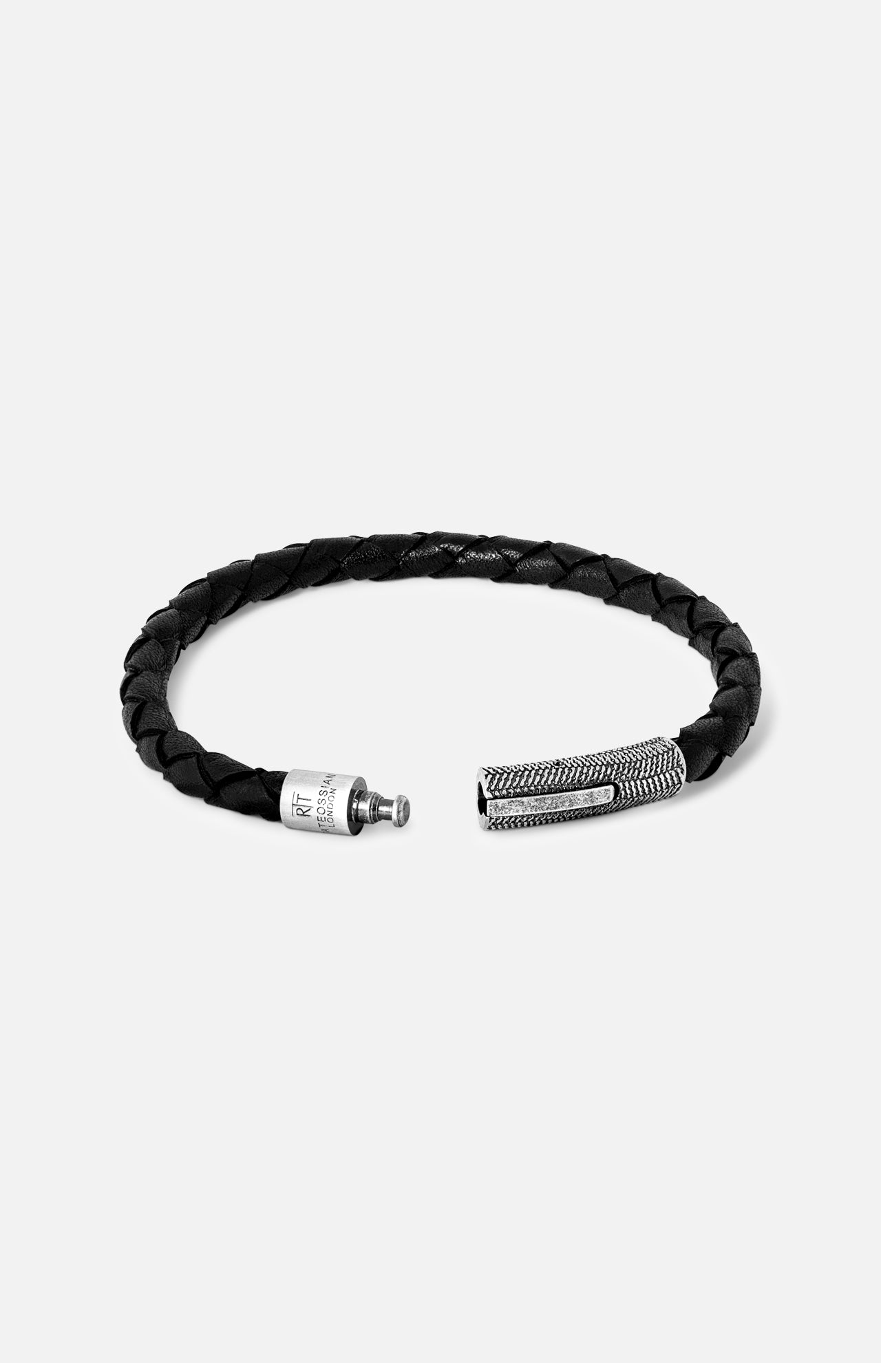 The TATEOSSIAN Vintage Herringbone Click Bracelet features black braided leather and a textured stainless steel clasp, displayed open against a plain light gray background—a sophisticated men's luxury accessory.