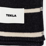 Folded black TEKLA Striped Lambswool Blanket with cream stripes and a white brand label.