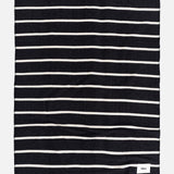 A rectangular TEKLA Striped Lambswool Blanket with dark navy and thin white horizontal stripes, featuring a small white logo tag in the bottom corner.
