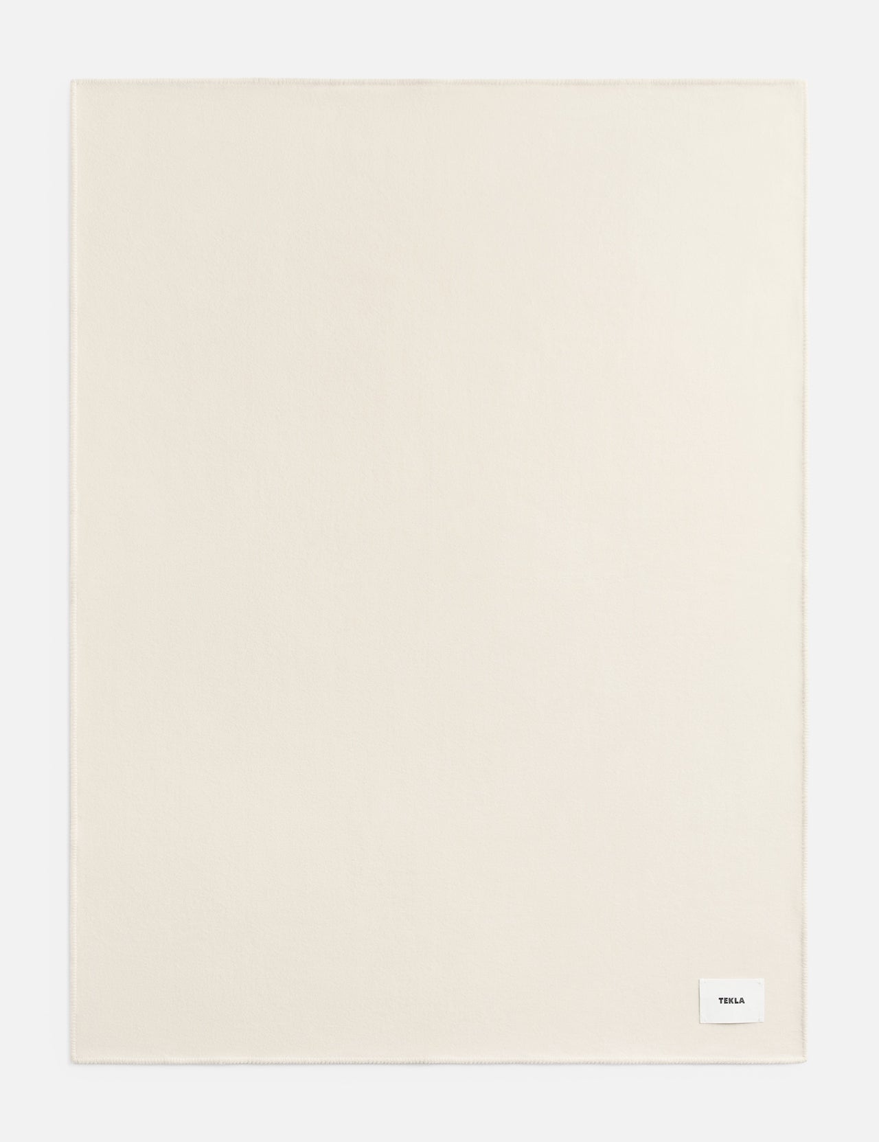 A rectangular off-white TEKLA Lambswool Blanket with a small white brand label in the bottom right corner.