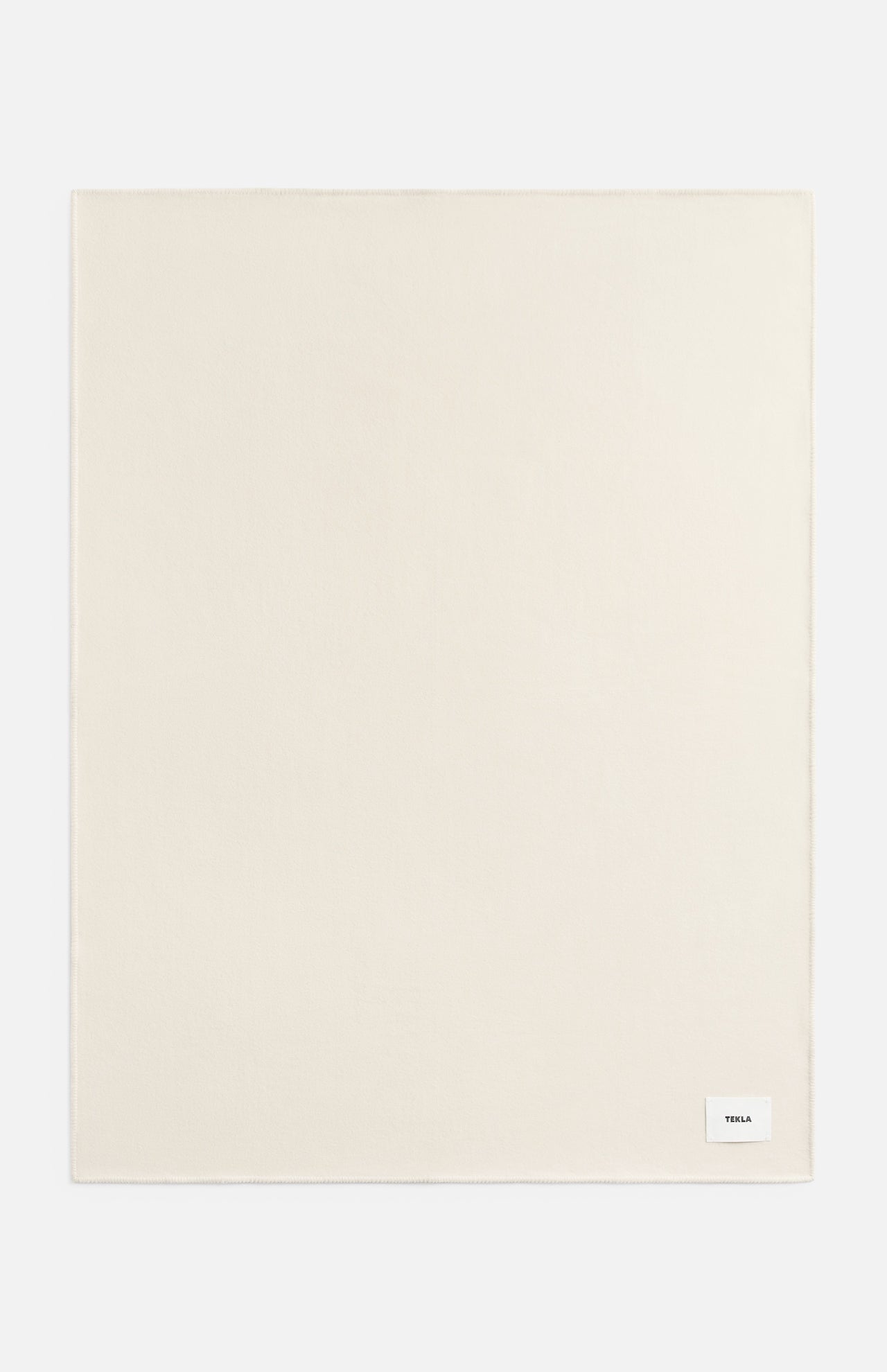 A rectangular off-white TEKLA Lambswool Blanket with a small white brand label in the bottom right corner.