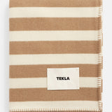 Folded TEKLA Striped Lambswool Blanket with wide beige and cream stripes and a stitched brand label on the front.