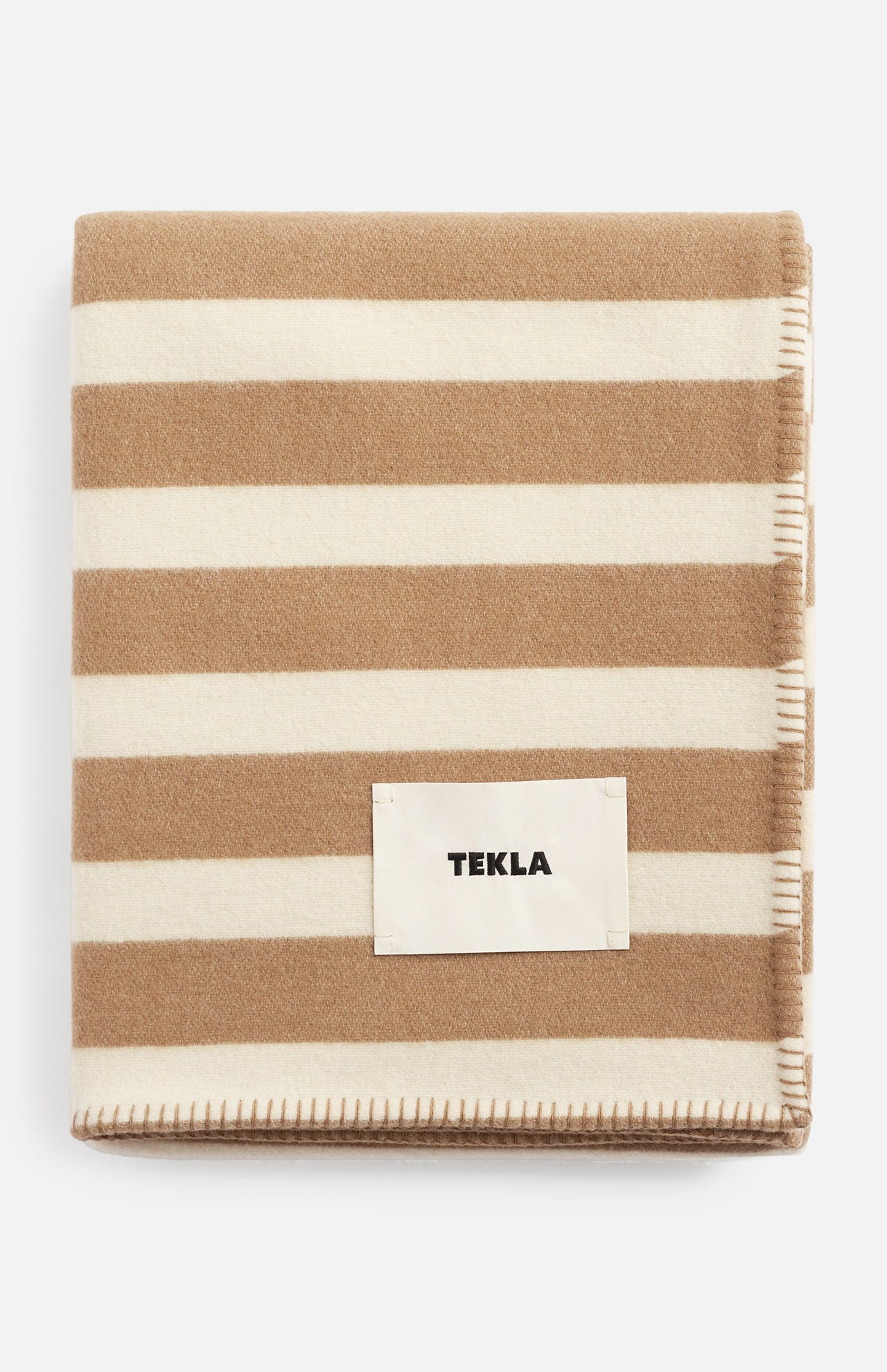 Folded TEKLA Striped Lambswool Blanket with wide beige and cream stripes and a stitched brand label on the front.
