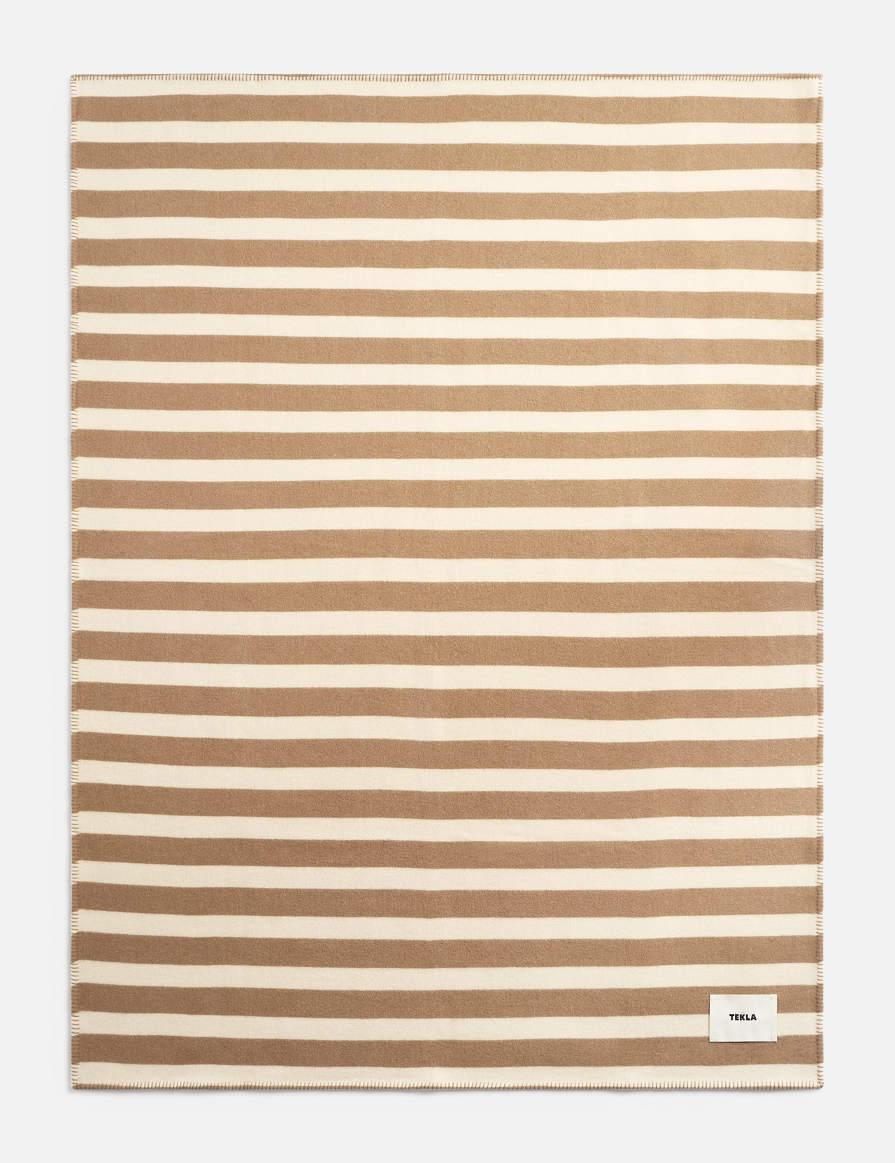 Rectangular TEKLA Striped Lambswool Blanket featuring horizontal tan and cream stripes with a small logo tag in the bottom corner.