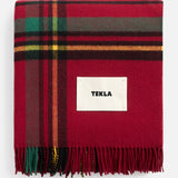 Red plaid TEKLA Lambswool Fringed Blanket with fringe and a central brand label, perfect for holiday decorating.