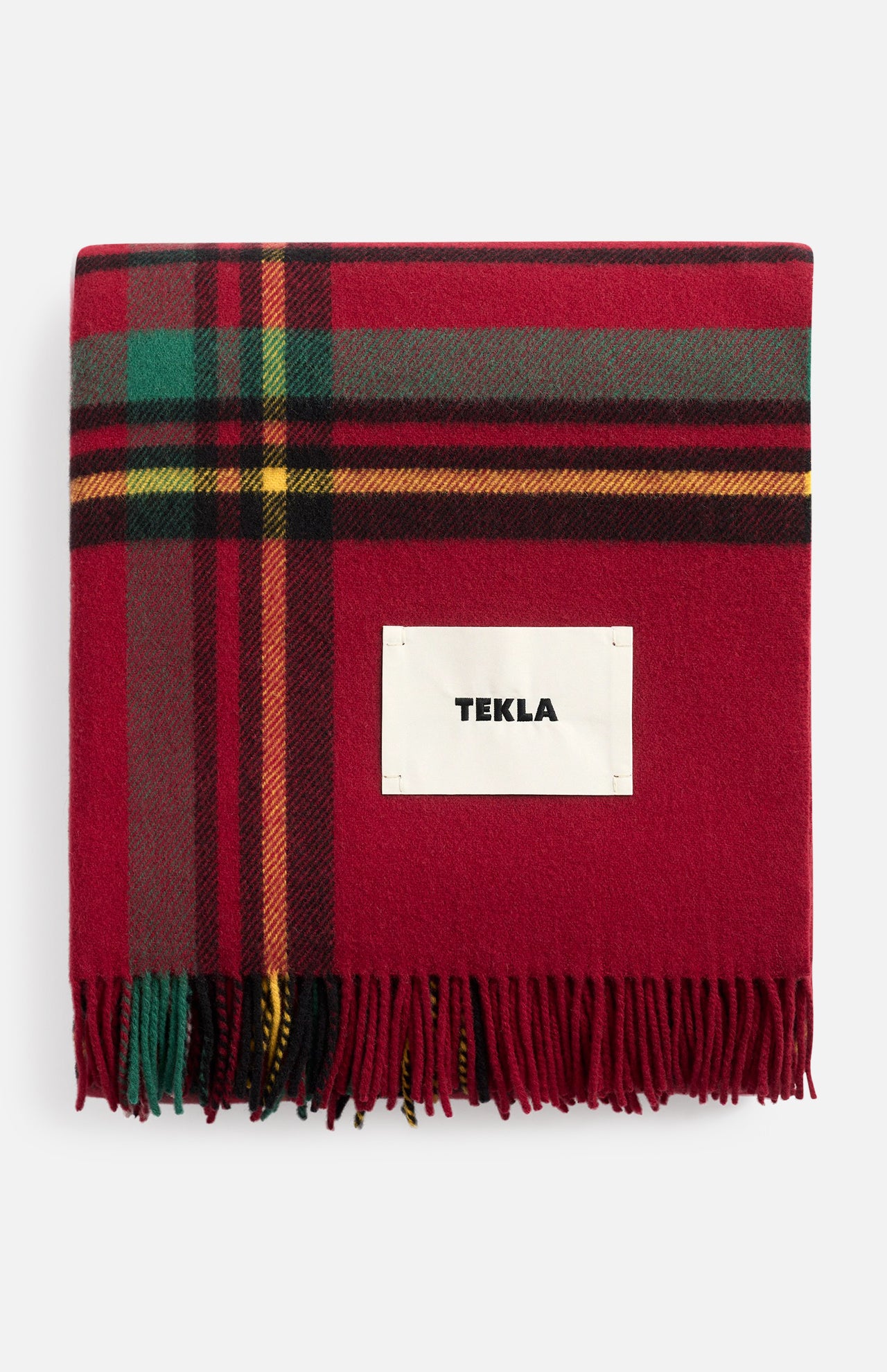 Red plaid TEKLA Lambswool Fringed Blanket with fringe and a central brand label, perfect for holiday decorating.
