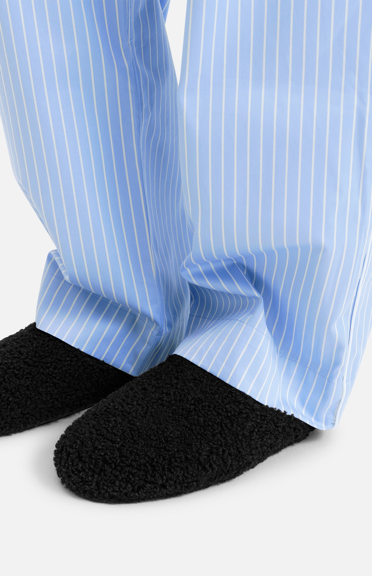 Black TEKLA Shearling Slippers with a cushioned footbed worn with light blue and white striped pajama pants.
