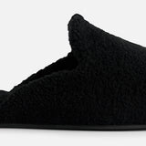 Side view of a black fuzzy TEKLA Shearling Slipper with a cushioned footbed.