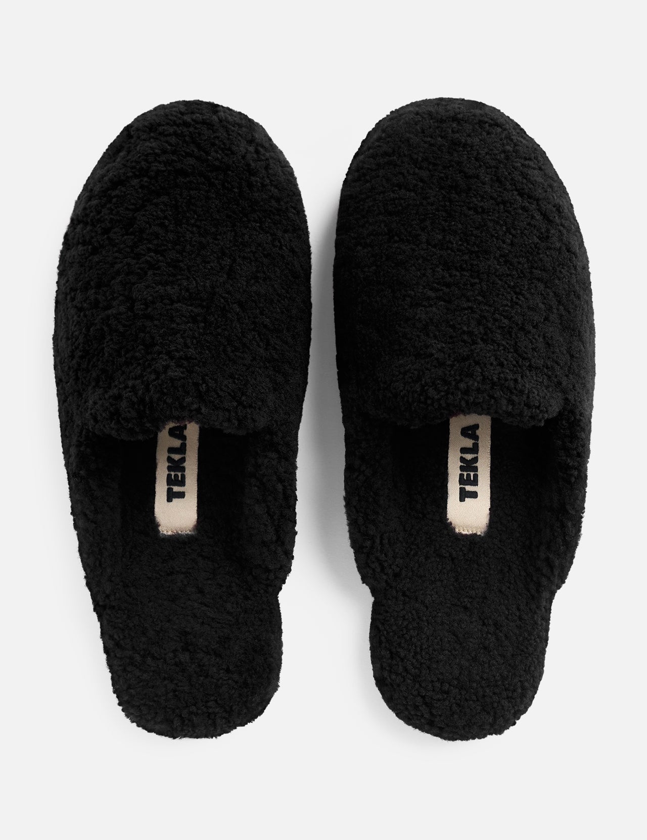 Pair of black TEKLA Shearling Slippers with logo tags on the cushioned footbeds.