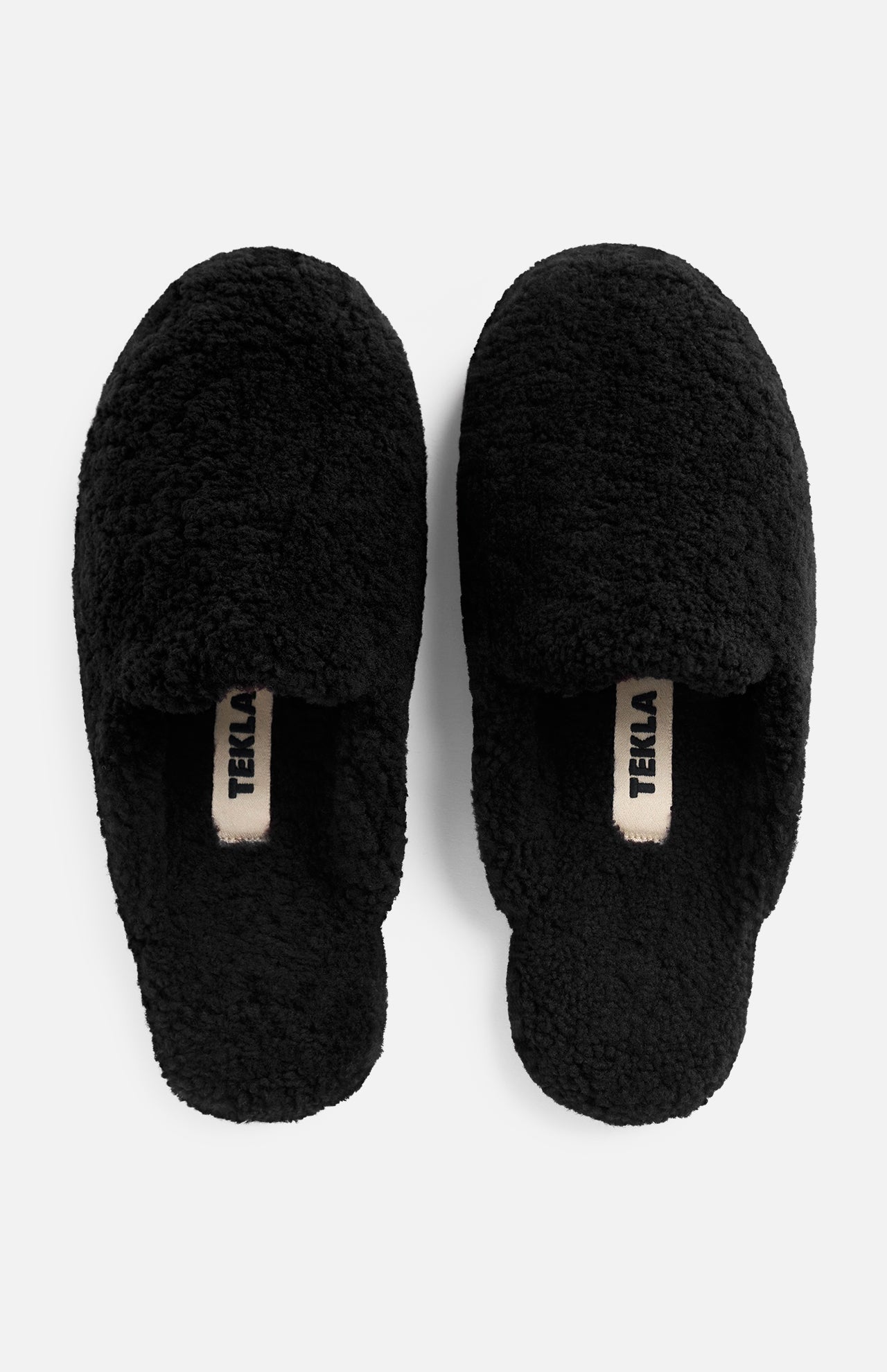 Pair of black TEKLA Shearling Slippers with logo tags on the cushioned footbeds.