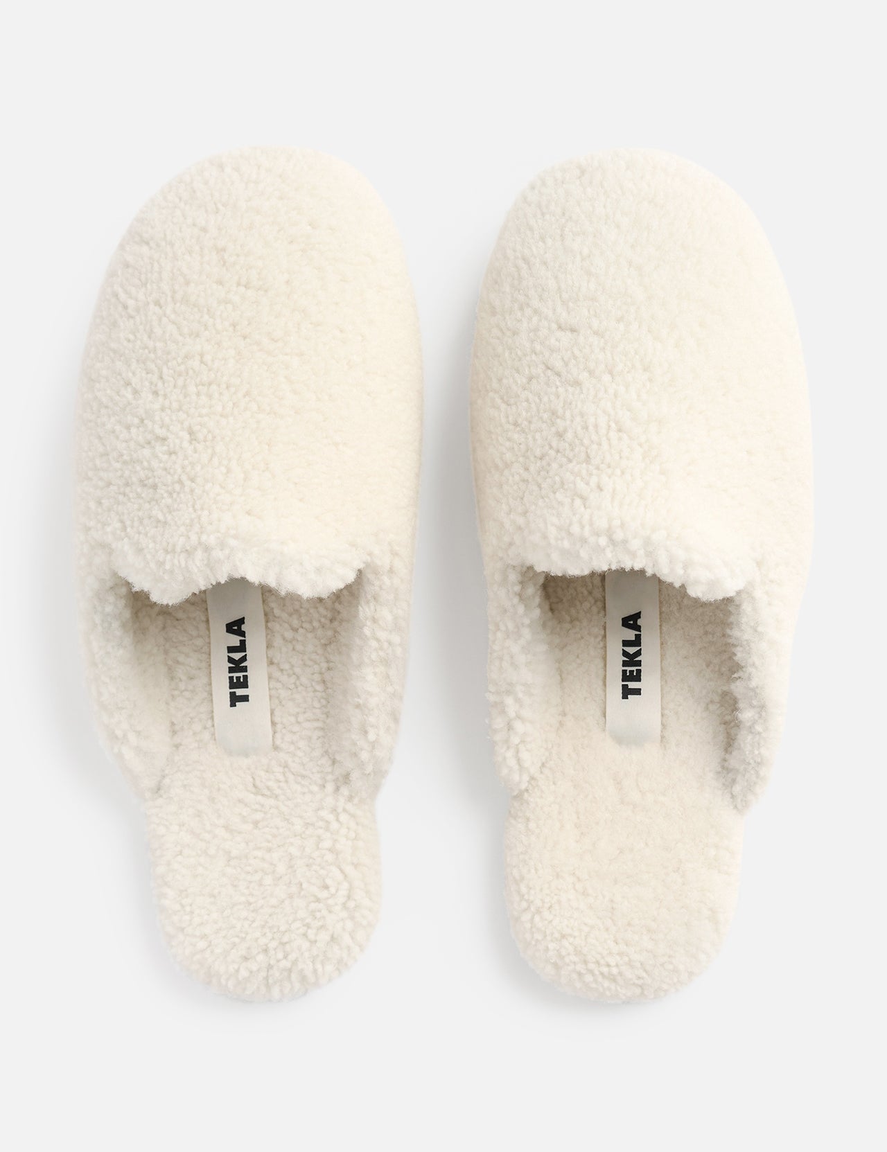 A pair of cream-colored TEKLA Shearling Slippers with a cushioned footbed, viewed from above.