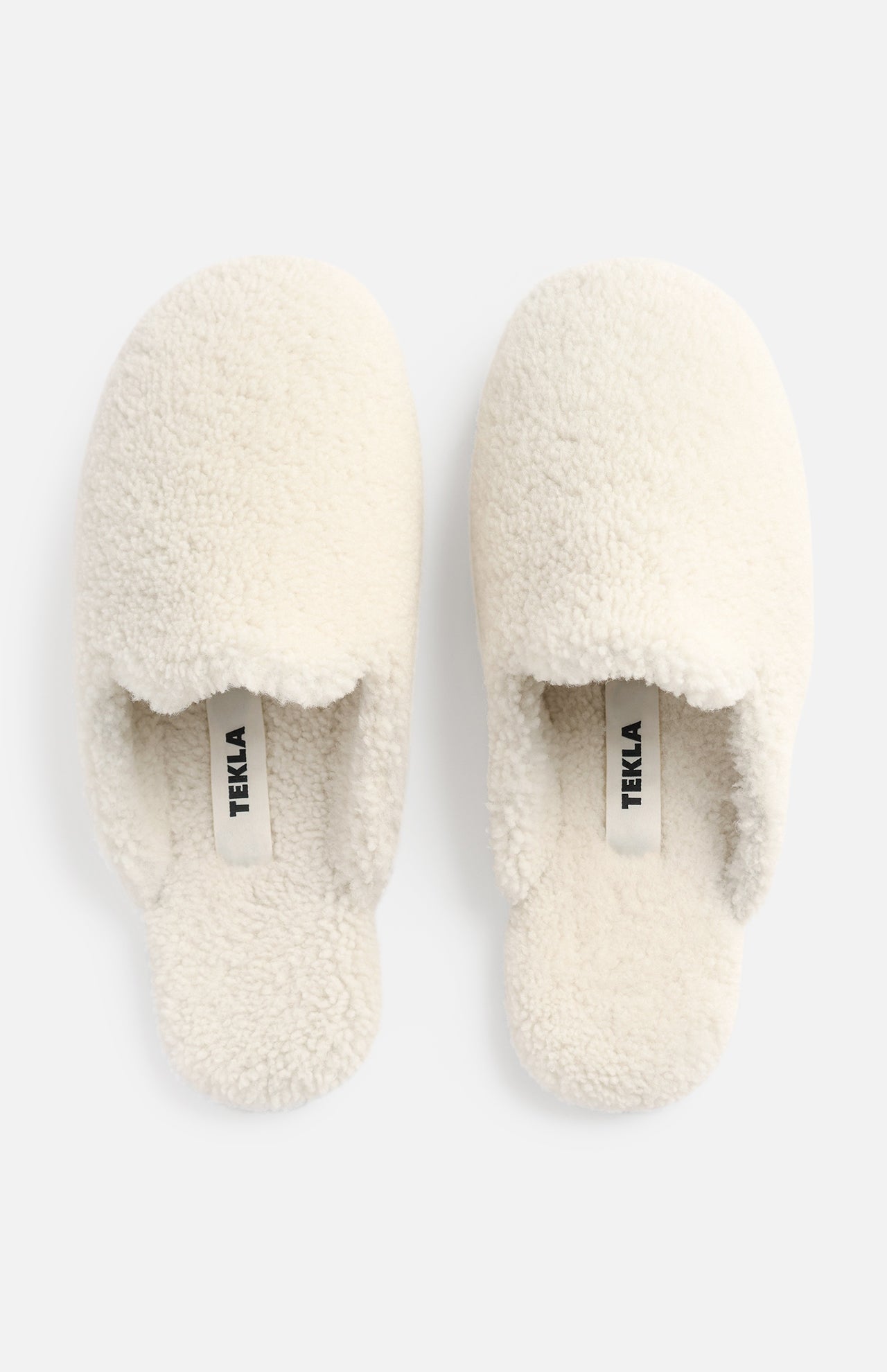 A pair of cream-colored TEKLA Shearling Slippers with a cushioned footbed, viewed from above.