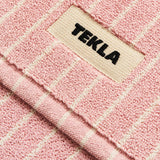 Pink and white striped textured organic cotton TEKLA Terry Bath Mat with a branded label in the center.