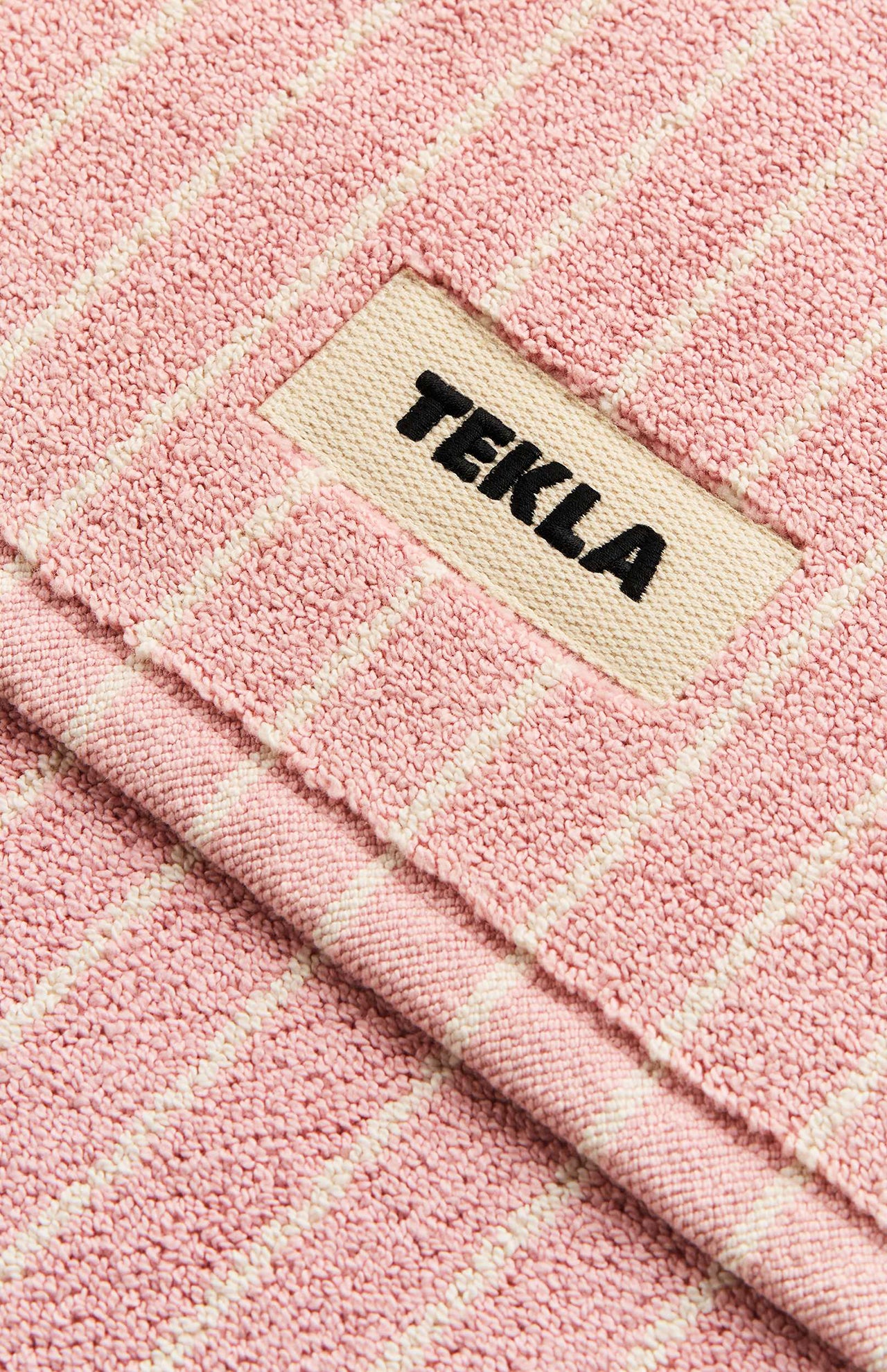 Pink and white striped textured organic cotton TEKLA Terry Bath Mat with a branded label in the center.