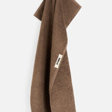 Brown organic cotton TEKLA Terry Bath Towel hanging from a loop with a brand tag.