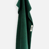 A forest green TEKLA Terry Bath Towel in organic cotton hanging from a loop.