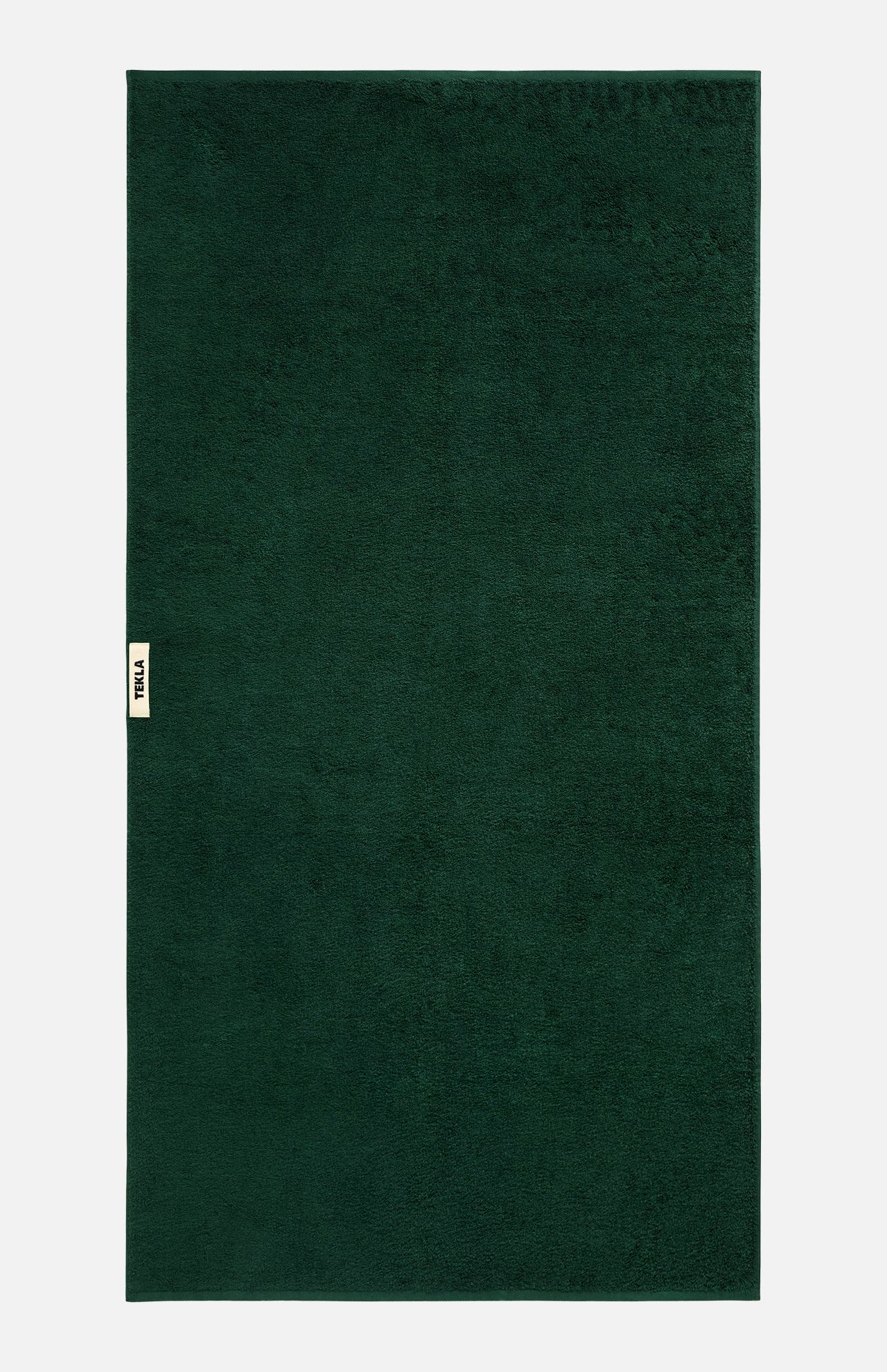 Rectangular forest green TEKLA Terry Bath Towel with a small branded fabric tab on the side.