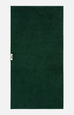 Rectangular forest green TEKLA Terry Bath Towel with a small branded fabric tab on the side.