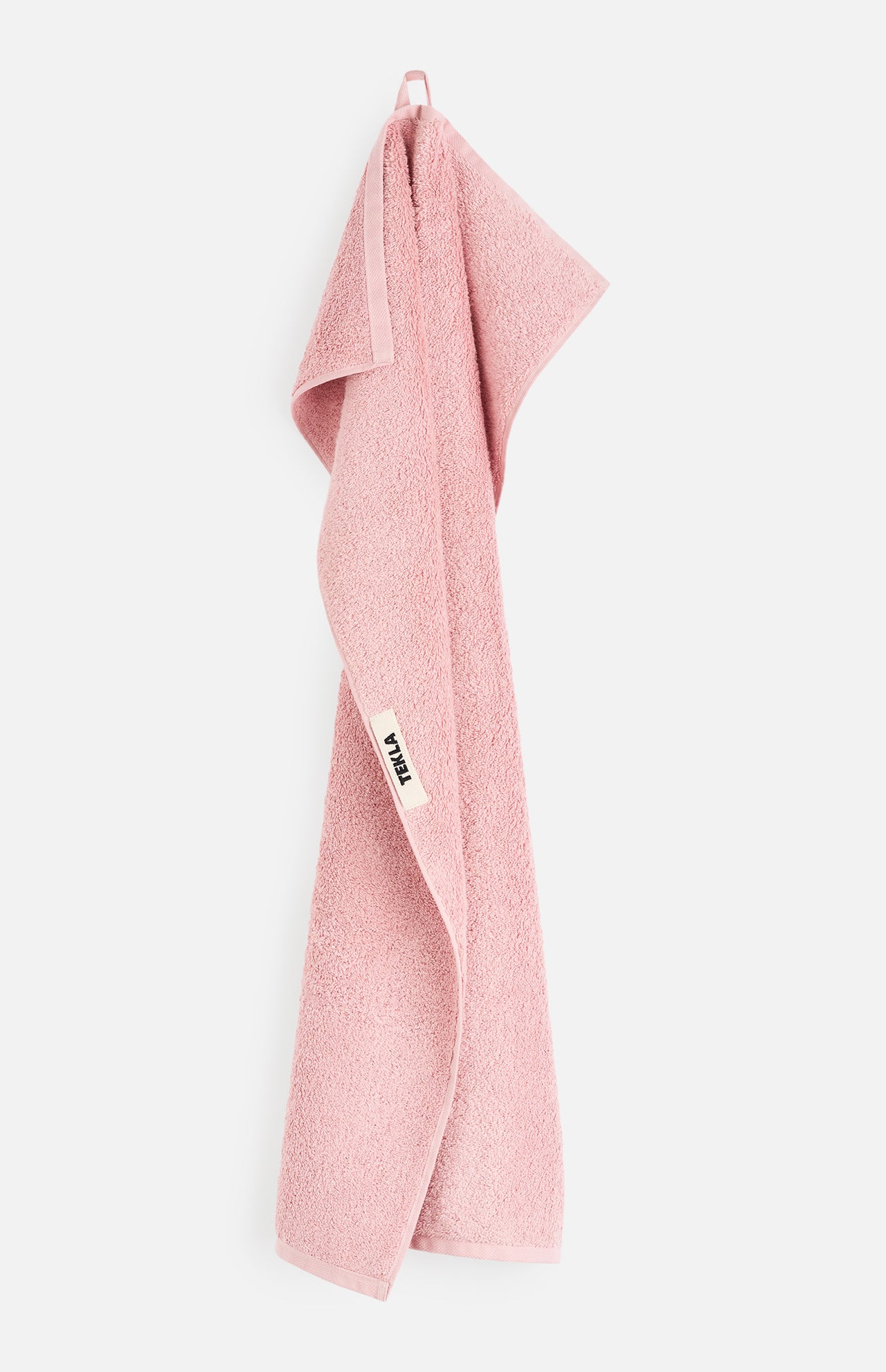 A pink organic cotton TEKLA Terry Bath Towel hanging from a loop.