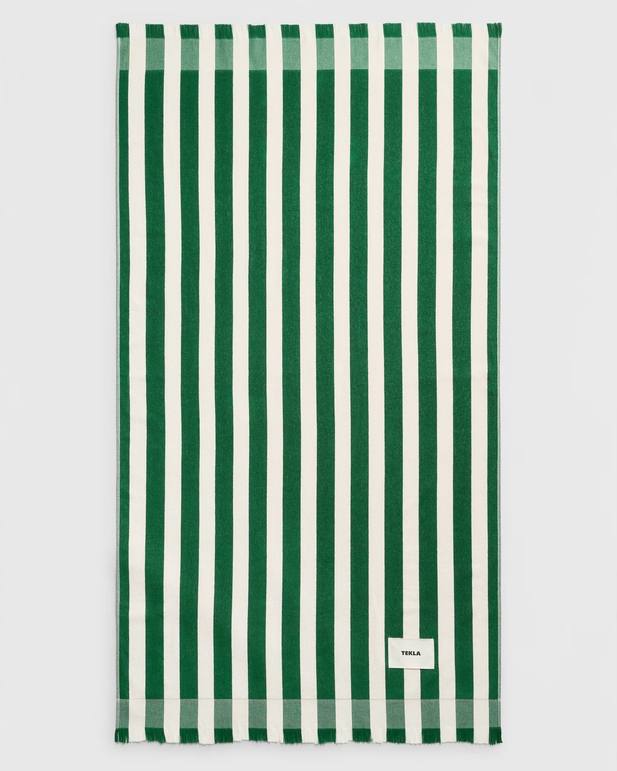 Rectangular dark green TEKLA Terry Beach Towel with alternating dark green and white vertical stripes and a small rectangular logo patch in the corner.