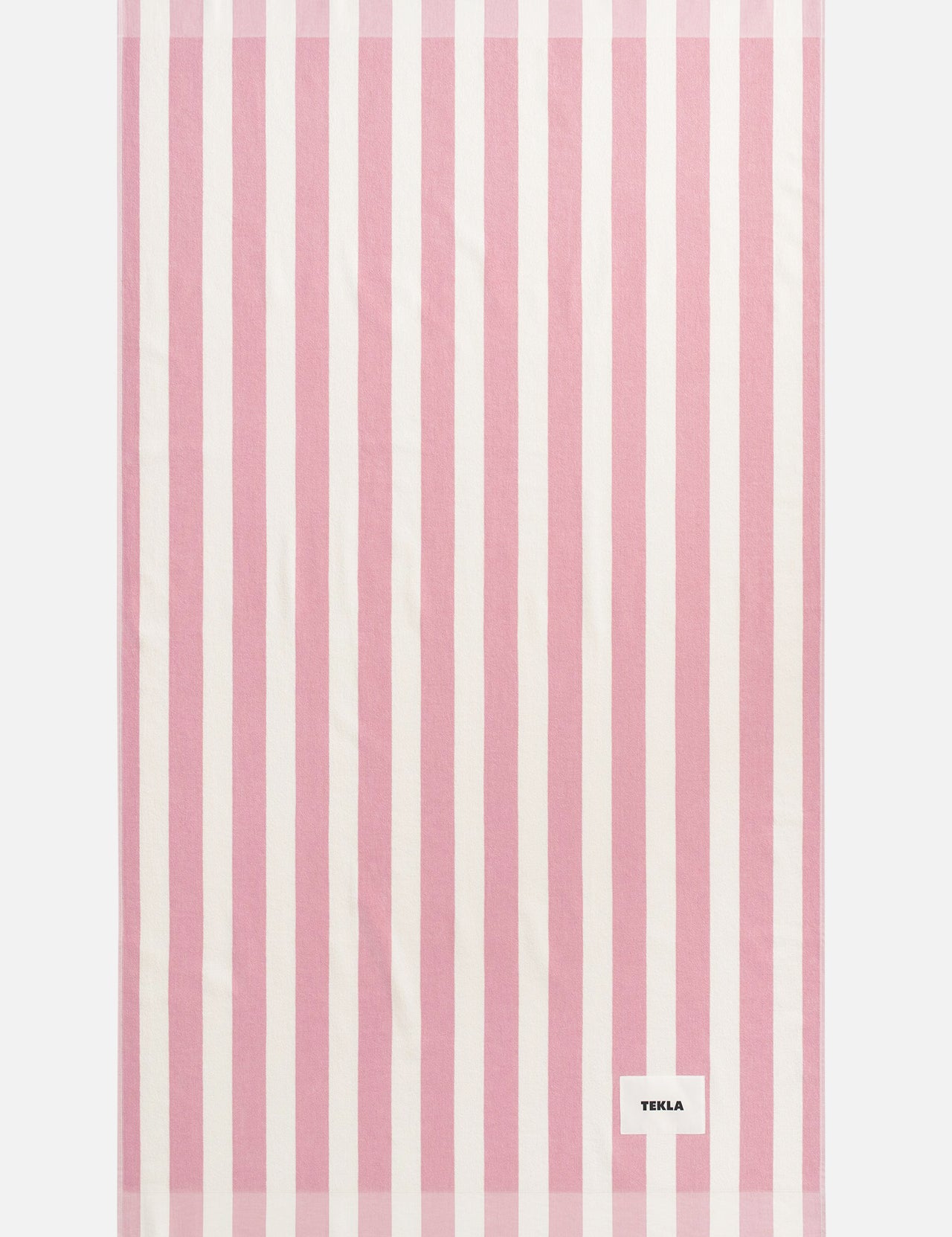 A rectangular pink TEKLA Terry Beach Towel with white vertical stripes and fringe at both ends.