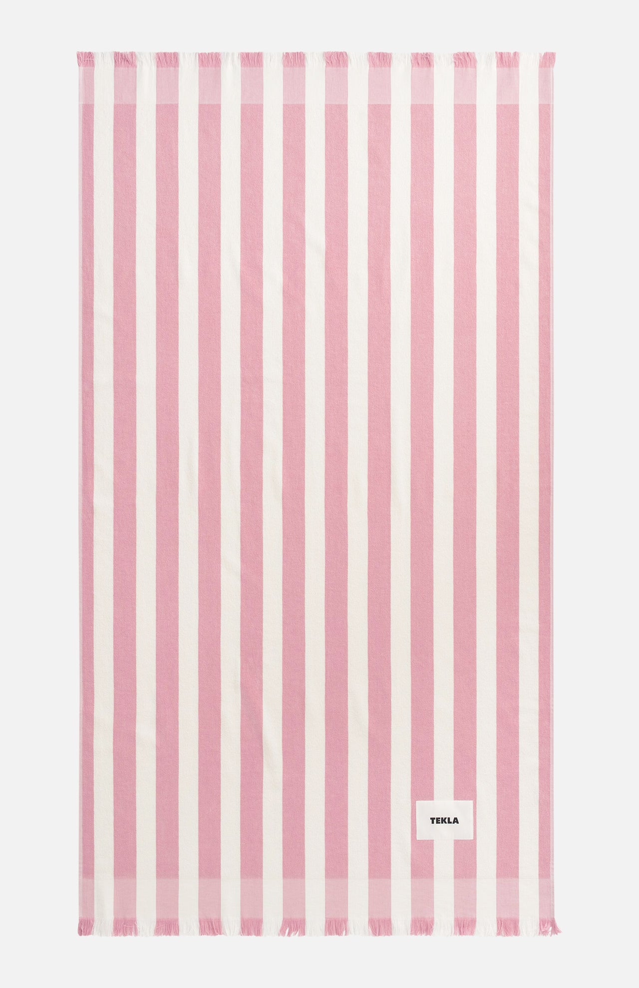 A rectangular pink TEKLA Terry Beach Towel with white vertical stripes and fringe at both ends.