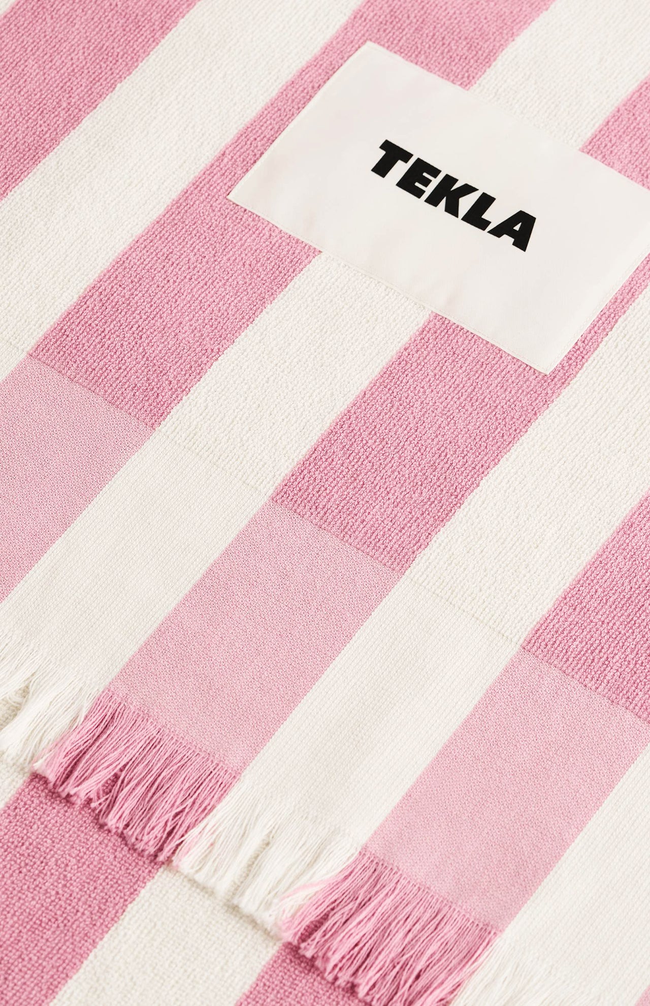 Pink and white striped fringed TEKLA Terry Beach Towel with a white logo patch.
