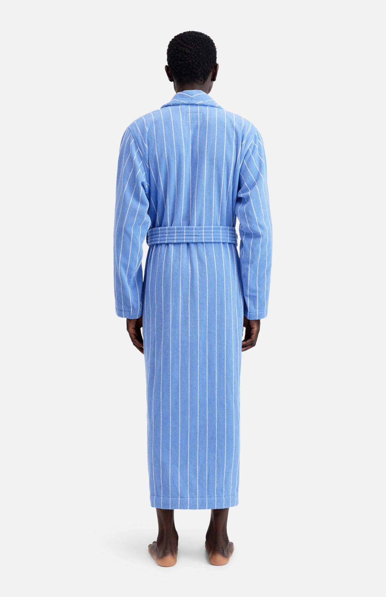 A person seen from the back wearing a blue, white-striped, tie-waist Terry Classic Unisex Bathrobe by TEKLA.