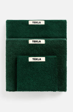 Three forest green TEKLA Terry Hand Towels of varying sizes stacked together, each featuring a white label with black text.