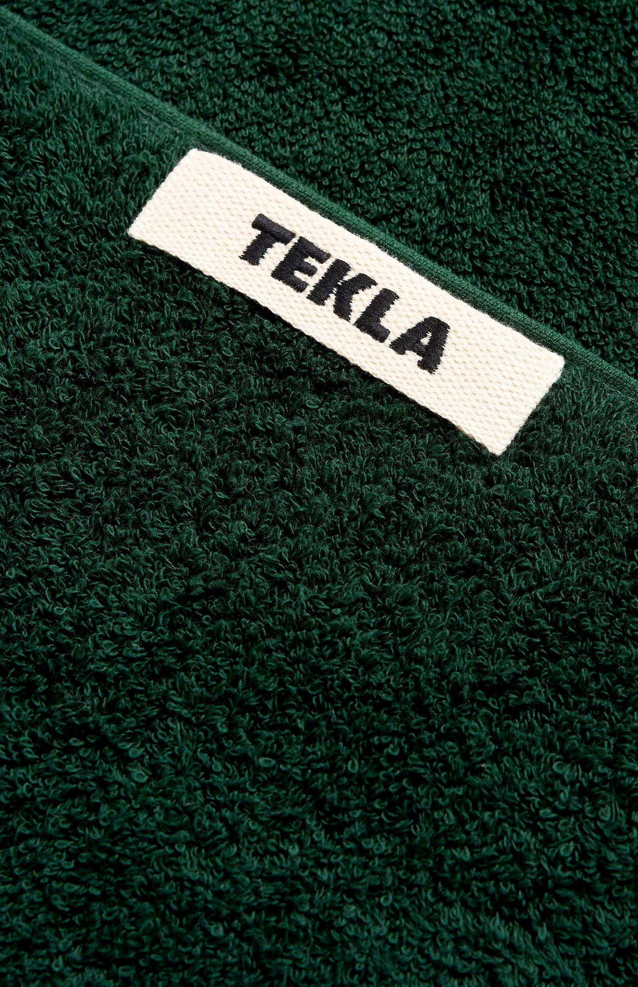 Forest green TEKLA Terry Hand Towel with a white rectangular tag featuring the brand name in black text.