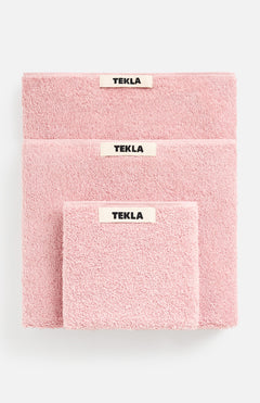 Three folded pink TEKLA Terry Hand Towels of varying sizes stacked on top of each other, each featuring a centered brand label.