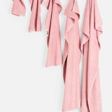 Five dusty pink organic cotton Terry Hand Towels of varying sizes hanging in a row against a white bathroom wall.