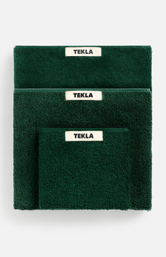 A stack of dark green organic cotton Terry Towel Washcloths in varying sizes, each featuring a white TEKLA brand label.