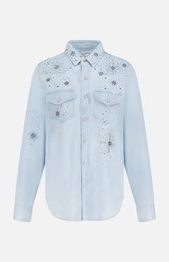 The All My Exes Beaded Shirt by MOTHER is a light blue Western denim shirt featuring long sleeves, pearl snap buttons, two chest pockets, and rhinestone star embellishments across the front, shoulders, and sleeves.