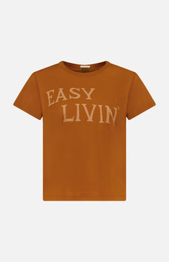 The Boxy Goodie Goodie T-shirt by MOTHER is a rust-colored, slim fit tee with short sleeves and “EASY LIVIN’” printed in large, light beige letters on the chest for a subtle vintage vibe.