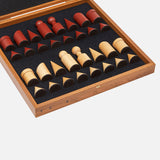 The Milos Terracotta Chess Game Set by THE CONRAN SHOP features handcrafted wooden pieces in red and natural tones with geometric forms, all housed in a wooden case with foam interior for a minimalist look.