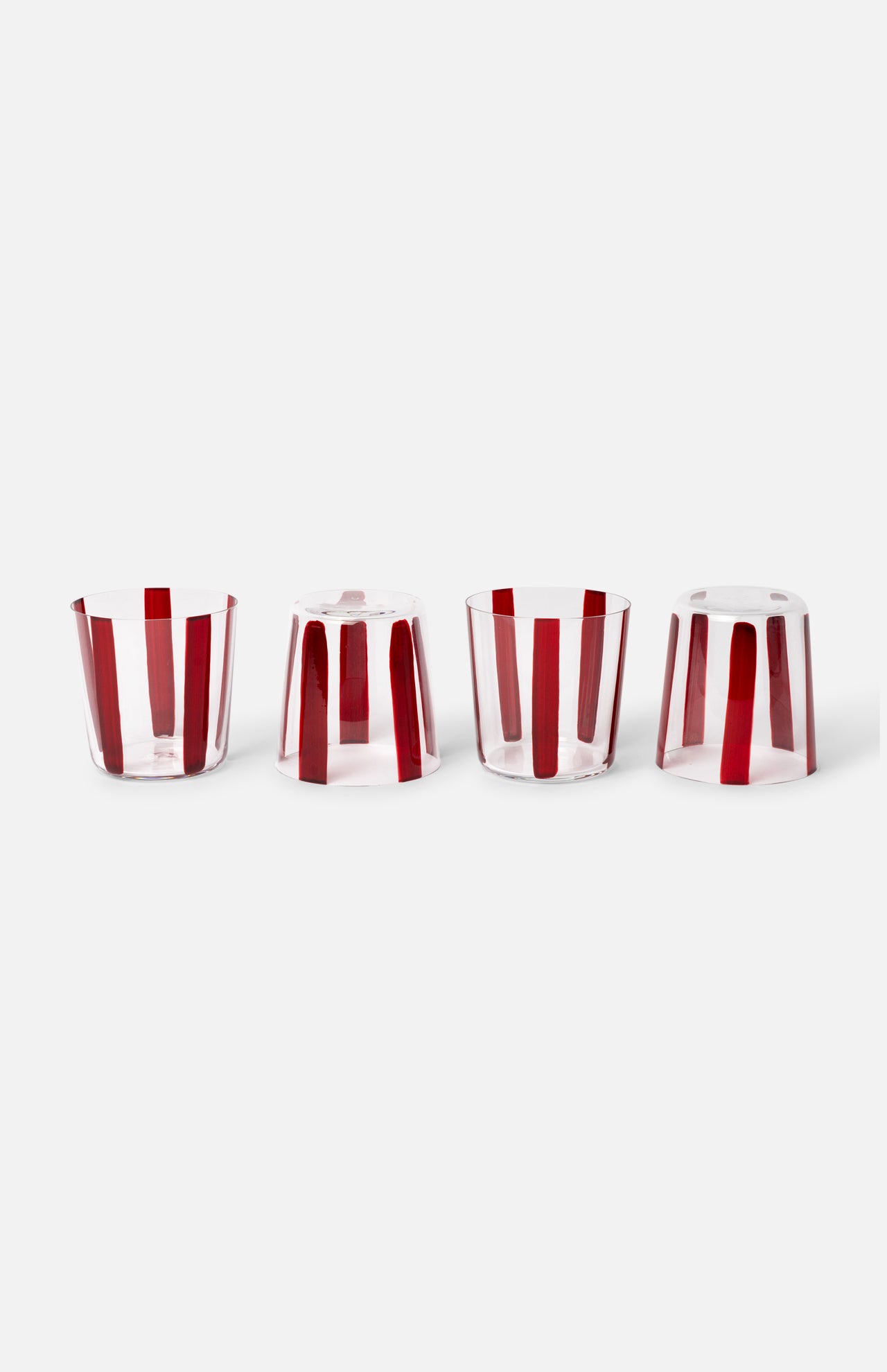 The Nova Stripe Tumbler Set of 4 by THE CONRAN SHOP features clear crystal glasses with vertical red stripes, arranged in a row on a white background; the rightmost tumbler is upside down, showcasing the striped design from another angle.